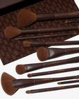 A set of 11 makeup brushes with brown handles and hypoallergenic synthetic bristles, displayed alongside a brown vegan magnetic brush clutch.
