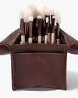 A set of twelve makeup brushes with beige handles and white bristles, displayed inside a brown vegan leather case.