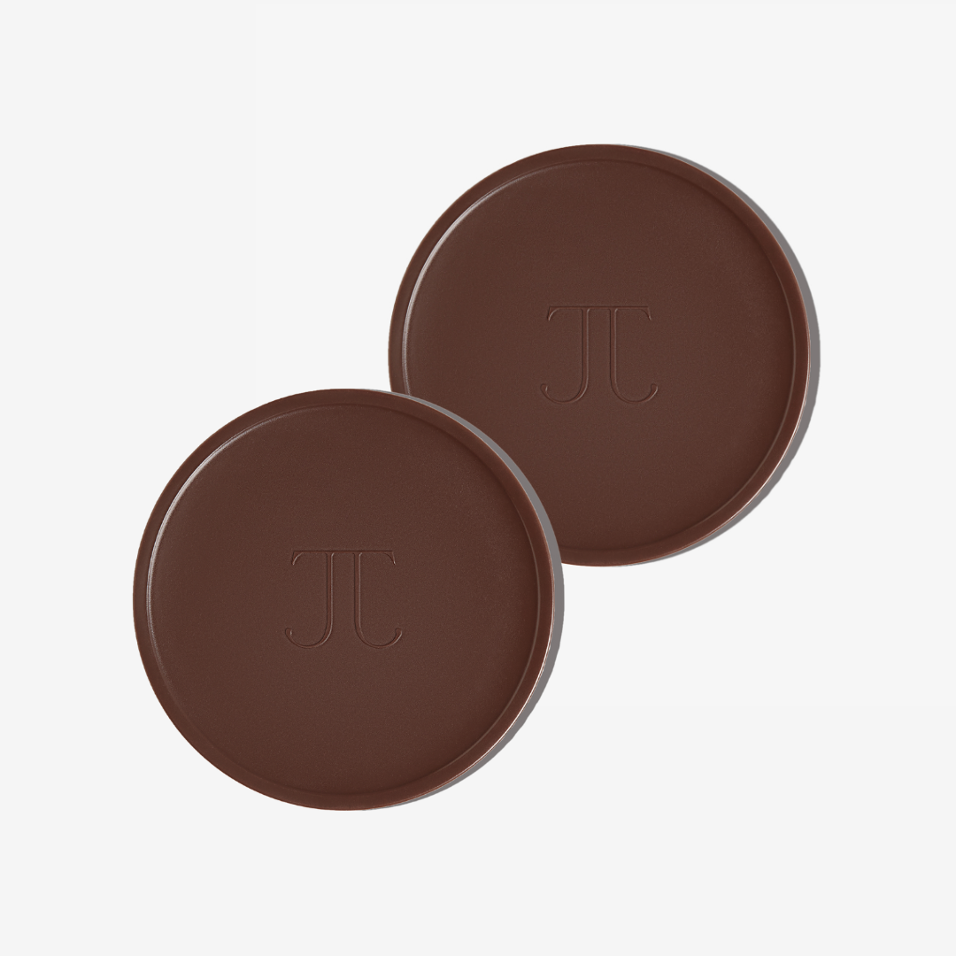 Two pans of Bronzour sun-kissed sculpt cream with a dark brown to dark bronze gradient, featuring the initials 'TJ' on each pan.