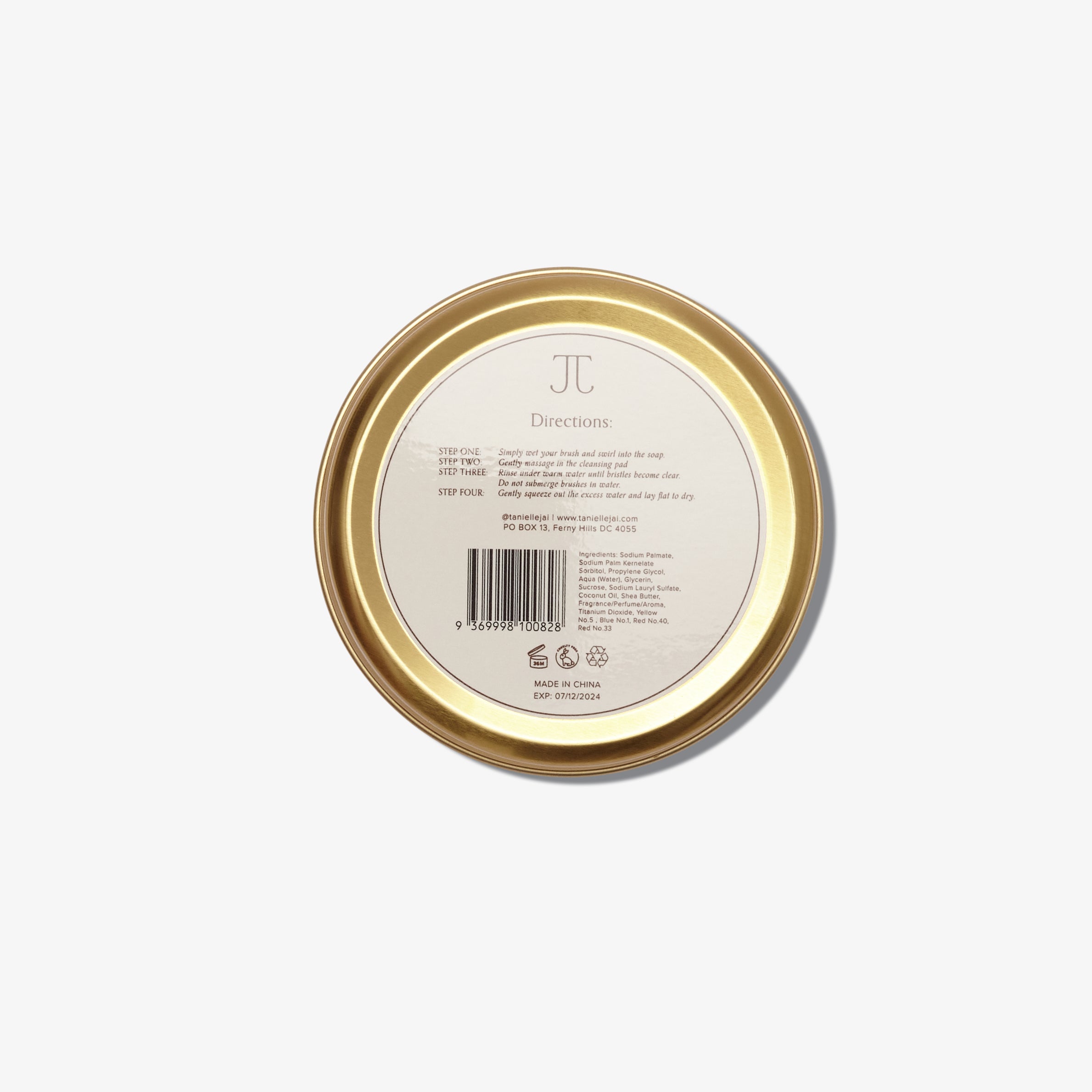 A round container of Tanielle Jai brush soap with a silicone cleansing pad inside. The label has information such as ingredients, directions and contact info