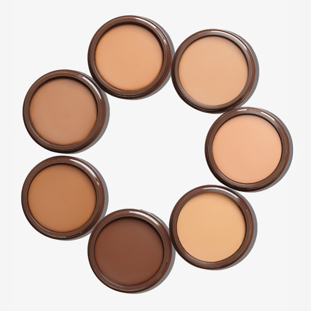 A set of seven round compact pans of Tanielle Jais Bronzour Cream bronzer in each shade, arranged in a circle.
