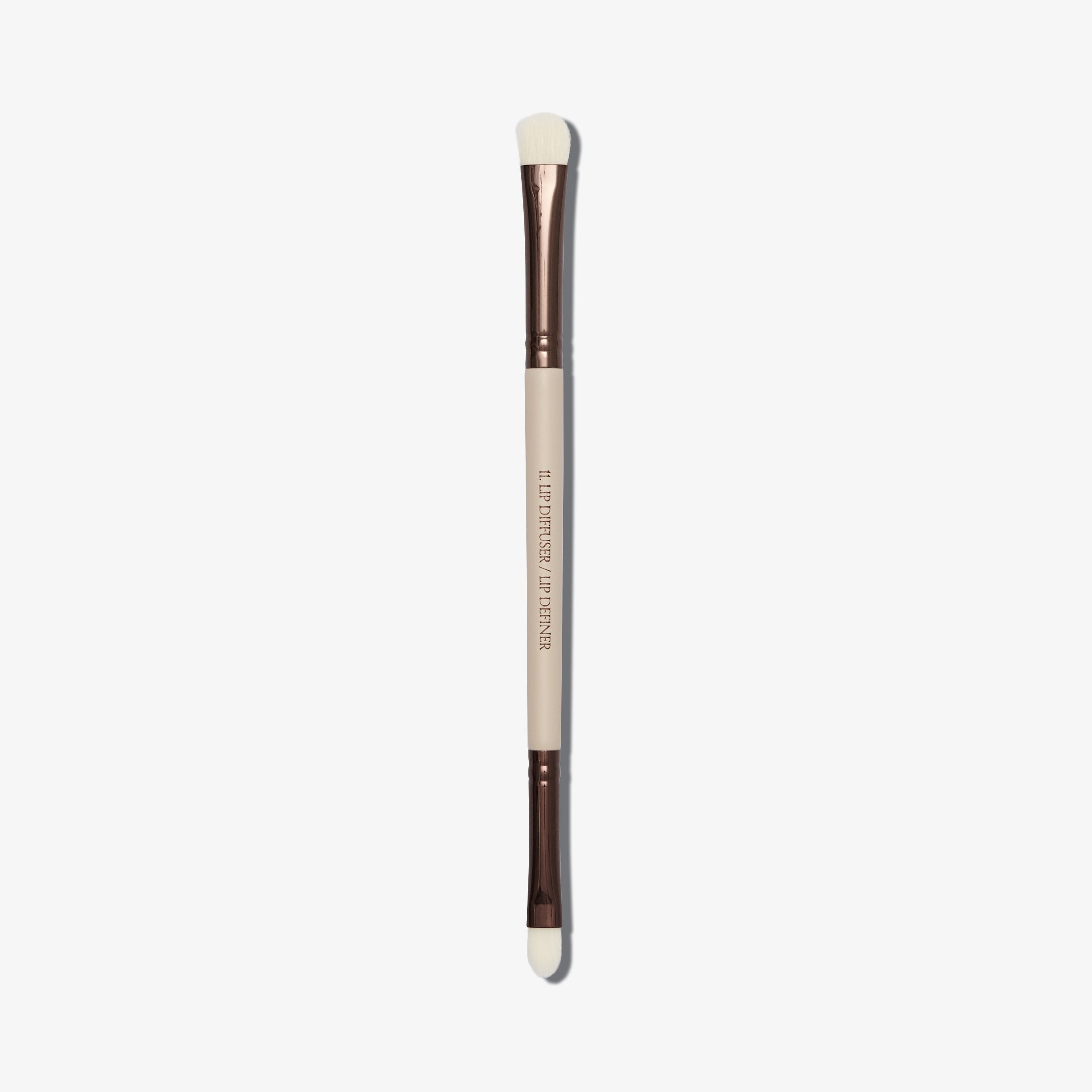 A dual-ended makeup brush with a beige handle and synthetic bristles, one end flat and wide, and the other end rounded for lip definition.
