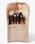 A set of twelve makeup brushes with beige handles and white bristles, displayed inside a cream vegan leather case. 