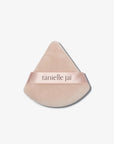 A triangular pink velvet powder puff with the logo 'tanielle jai' written across the center.